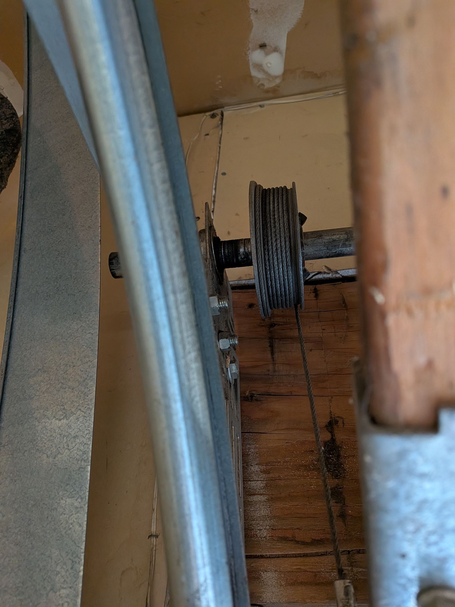 A low-angle view of a garage door cable spool and metal track attached to wooden framing.