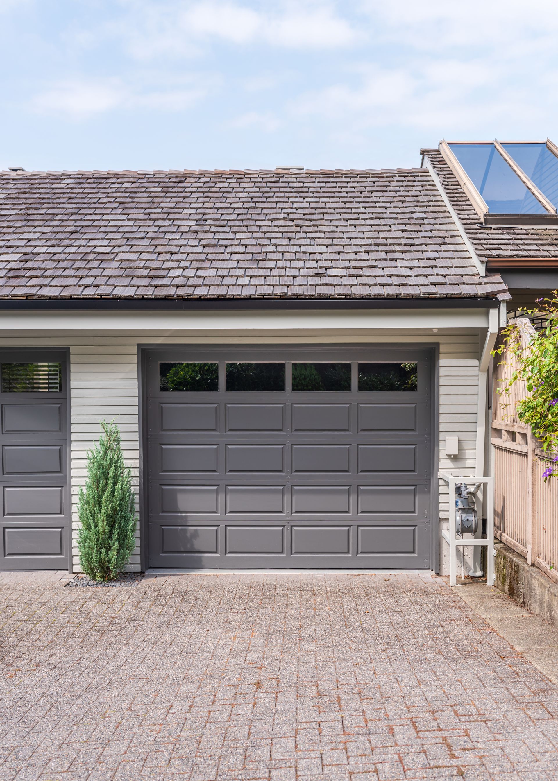 Gray garage door with window panels and a wooden shingle roof, set in front of a gravel driveway.