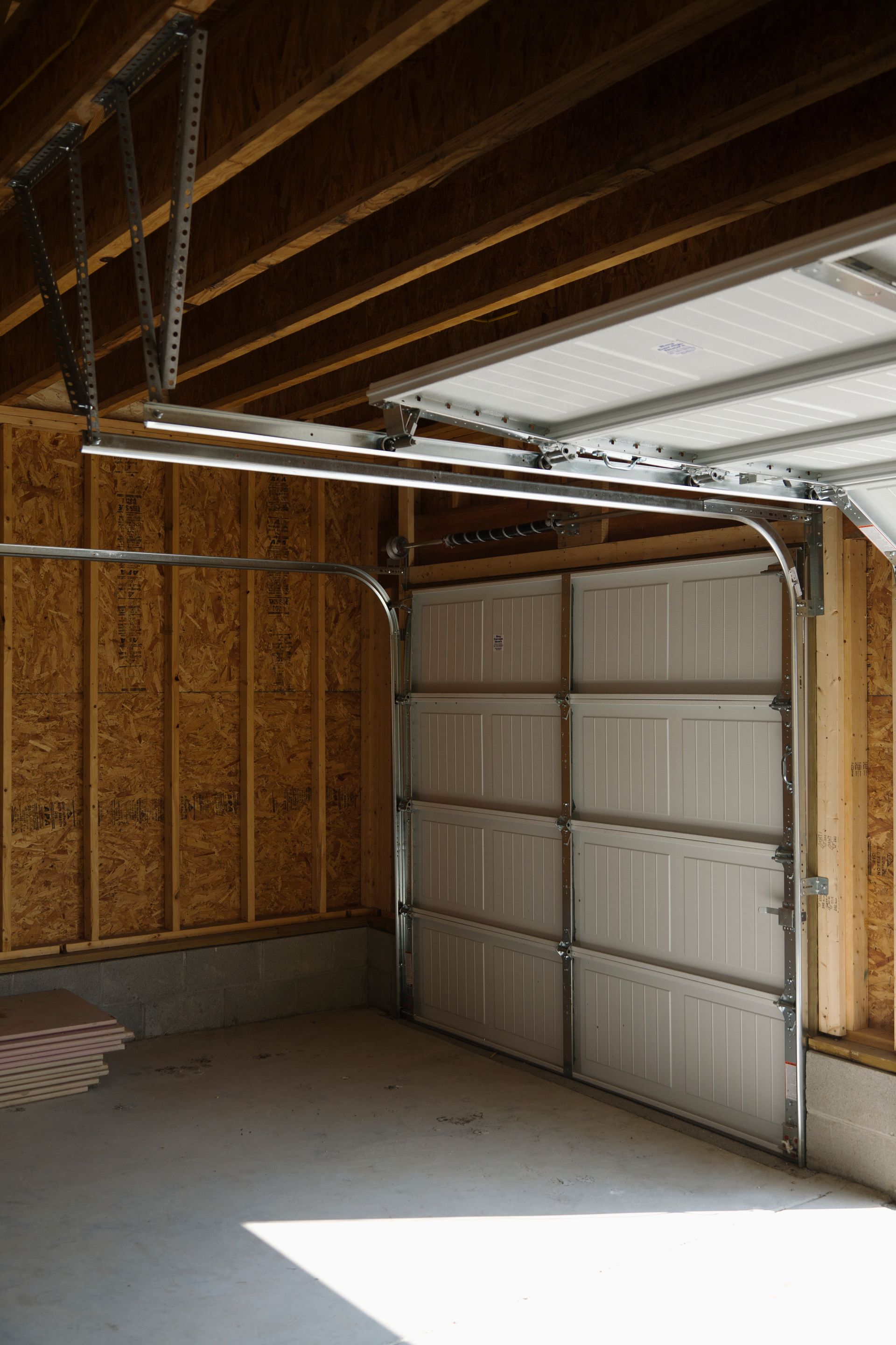 A white sectional garage door in a garage with unfinished wooden wall studs and a concrete floor.
