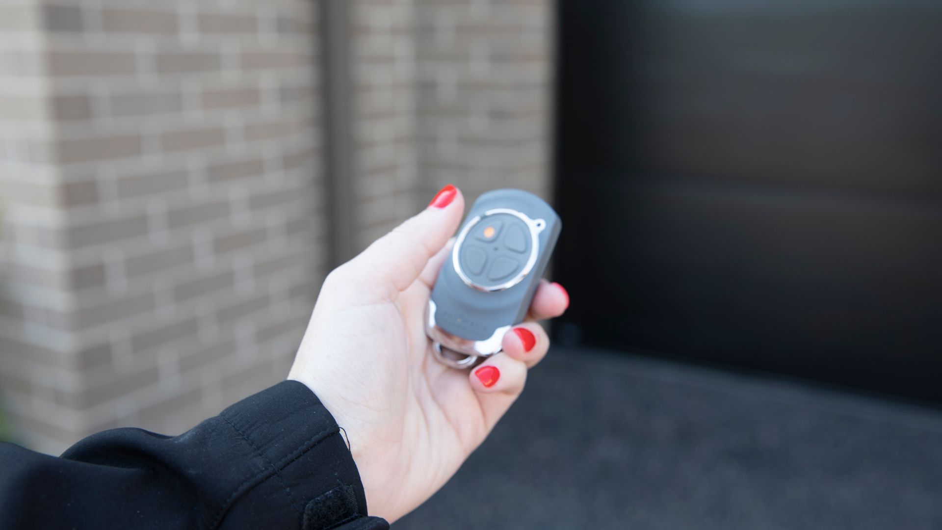 Hand holding a remote toward a garage door opening onto a parked black car