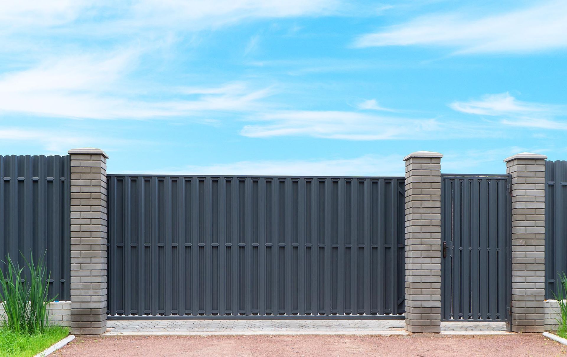 Modern gray metal fence with brick pillars under a blue sky