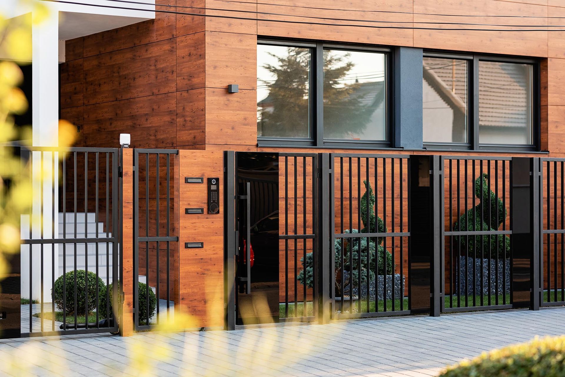 Modern brick house with black metal fence, large windows, and potted plants by the entrance