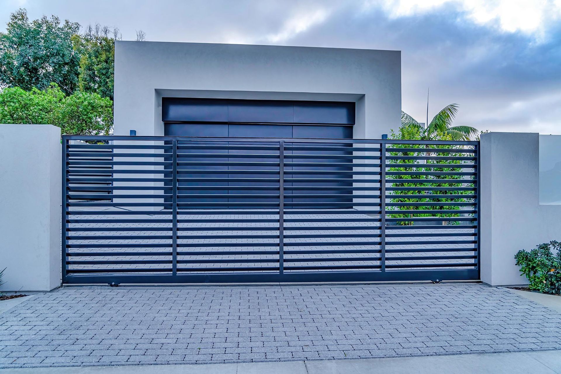 Modern house entrance with gray metal gate and driveway under a cloudy sky