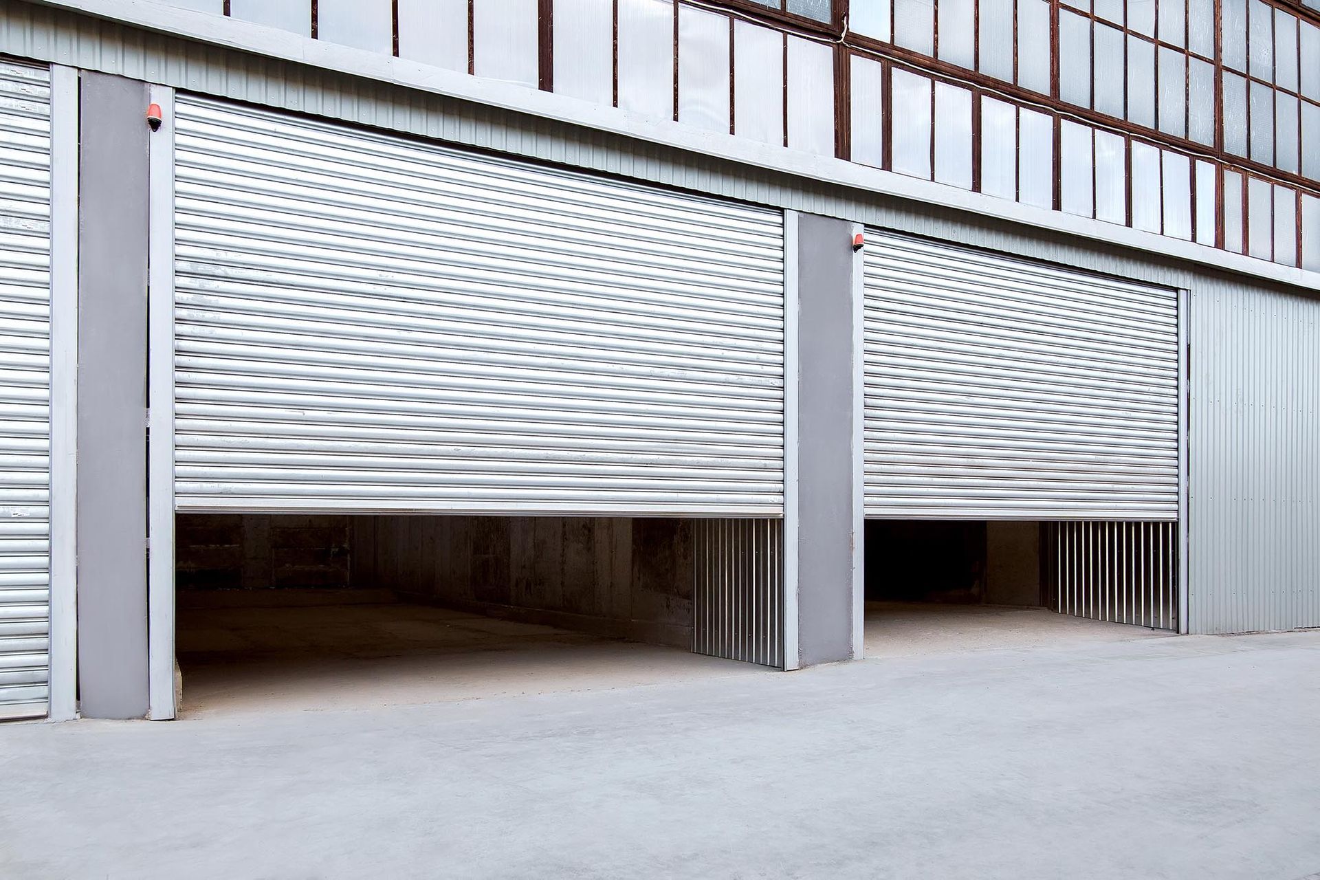 Two white metal roll-up garage doors, partially open on a commercial building exterior.