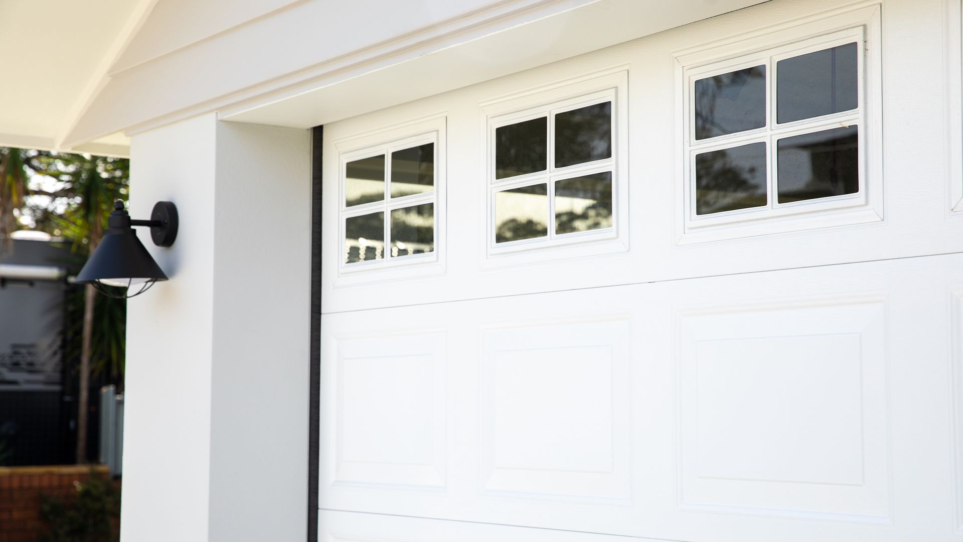 Suburban house exterior with beige siding, white garage doors, and landscaped front yard.