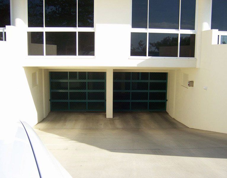 Modern building facade with a two-bay garage and large windows above, seen from a driveway