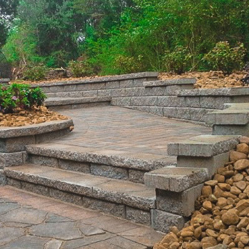 Stone steps and a paved patio are nestled into a landscaped backyard, framed by low stone retaining walls and rock beds.