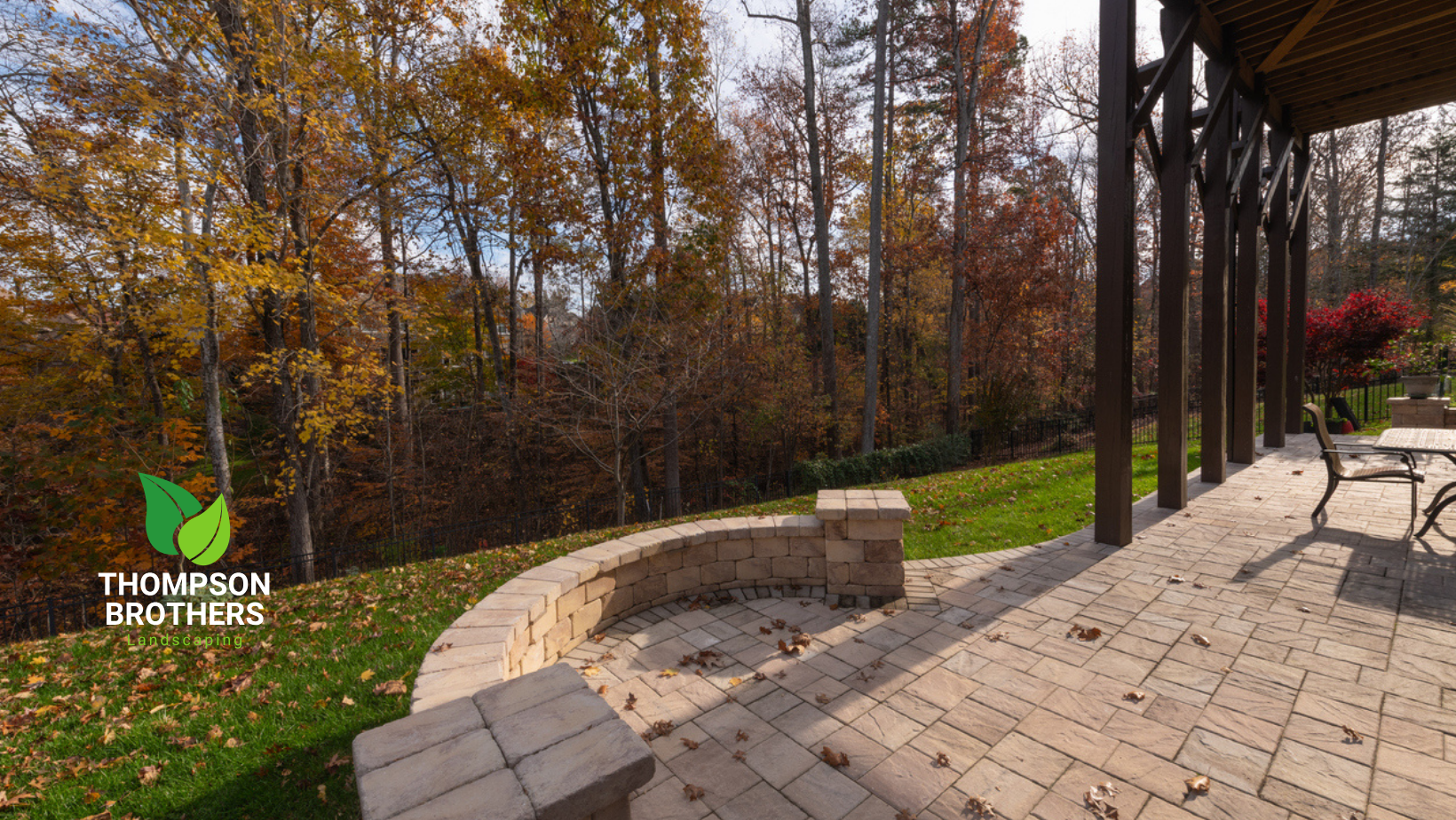 Brick patio with a fire pit, overlooking a grassy hill and autumn trees.