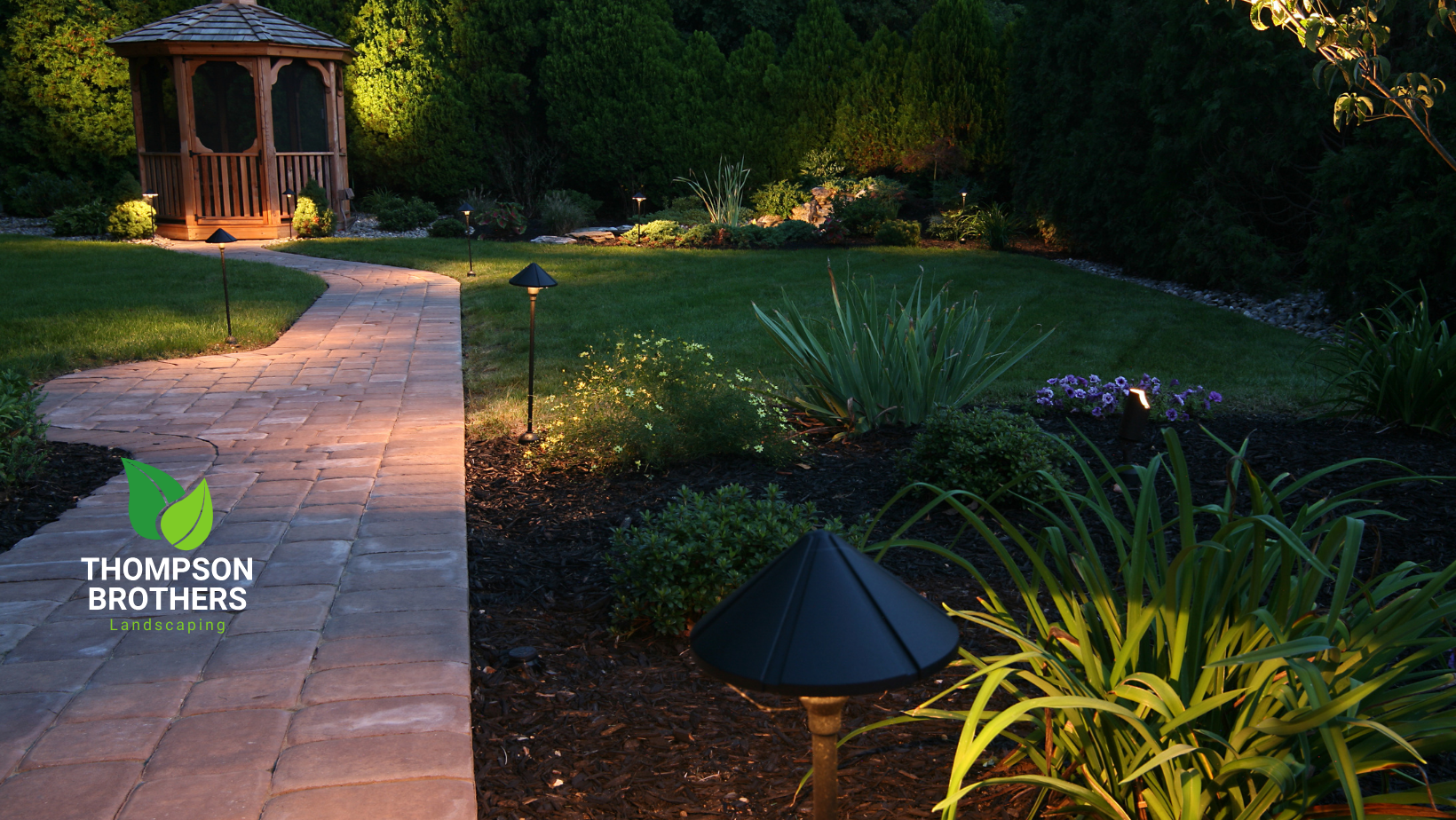 Pathway lit with landscape lights leading to a gazebo in a garden.