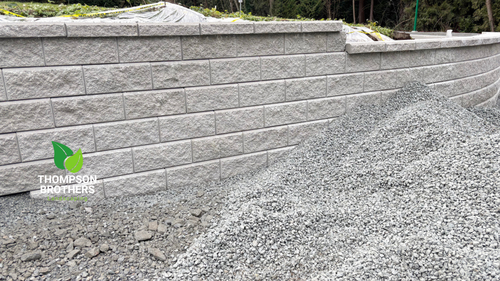 Gray retaining wall with a pile of gravel in front.