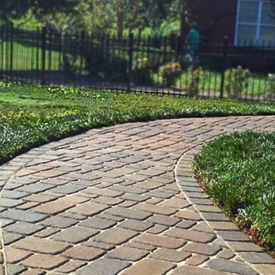 A curved stone paver walkway winds through a green lawn, edged with rectangular bricks, in a residential yard.