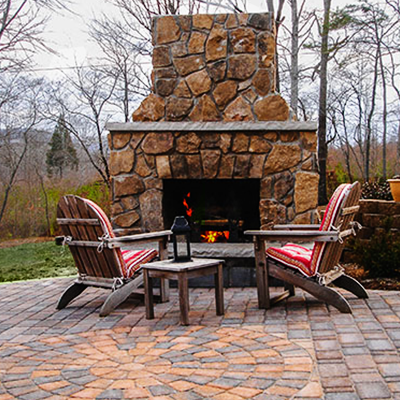 Fire pit with burning fire, stone patio, autumn trees, and lantern in the evening.