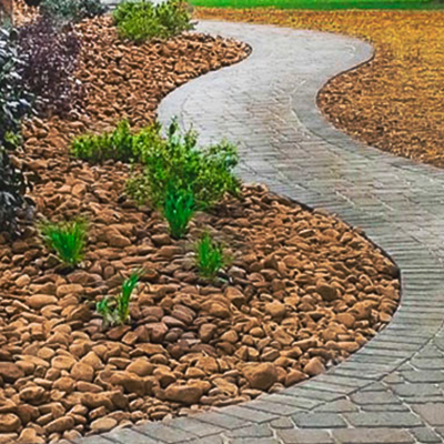 A curving paver stone walkway winds through a landscape of brown river rocks and small green shrubs.