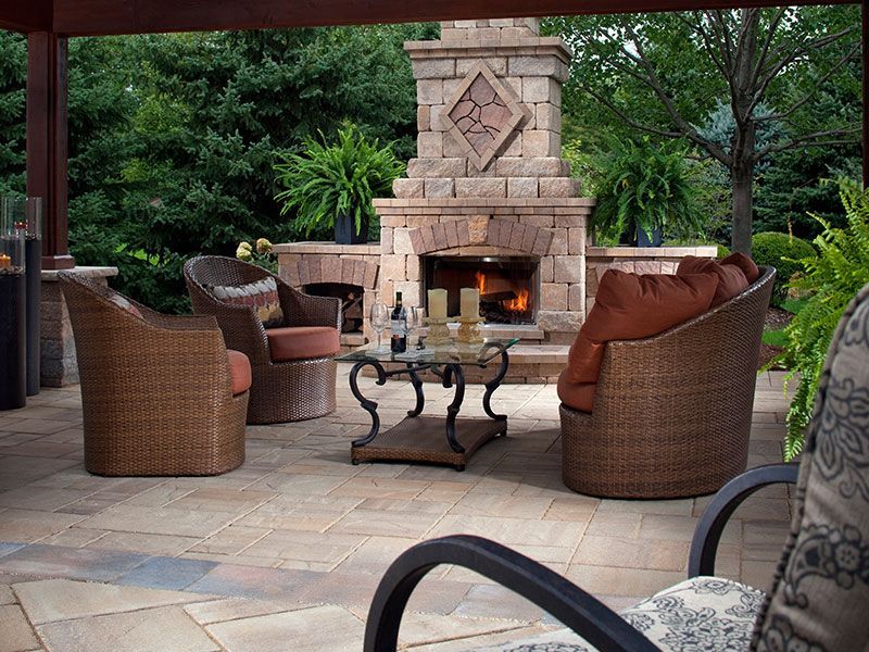 Cozy outdoor patio featuring a stone fireplace, wicker chairs, and a glass-topped table under a covered pergola.