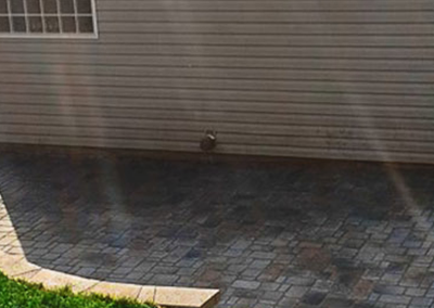 A multi-toned stone patio with a curved edge border set against a house with light-colored horizontal siding.