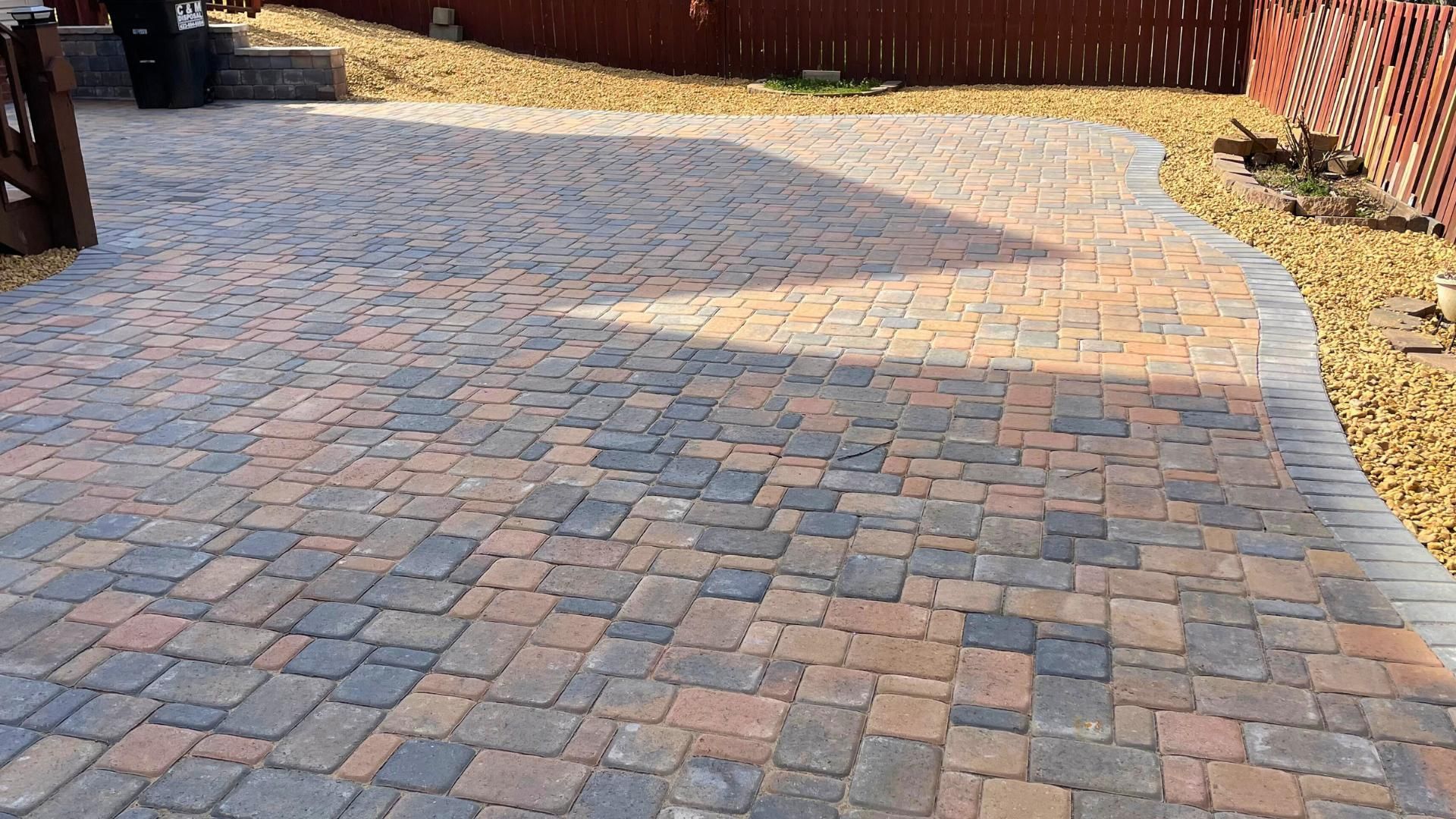 A patio made of multicolored rectangular concrete pavers in earth tones, featuring a darker gray stone border.