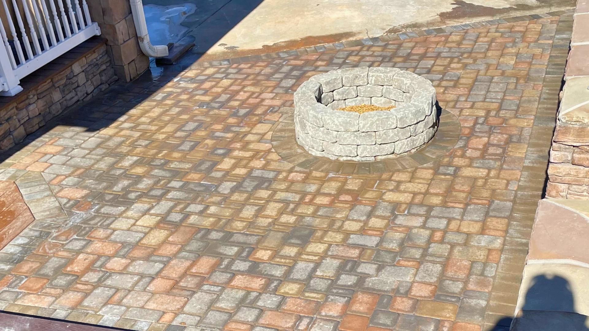 A stone fire pit sits in the center of a patio made of variegated, multi-colored brick pavers.