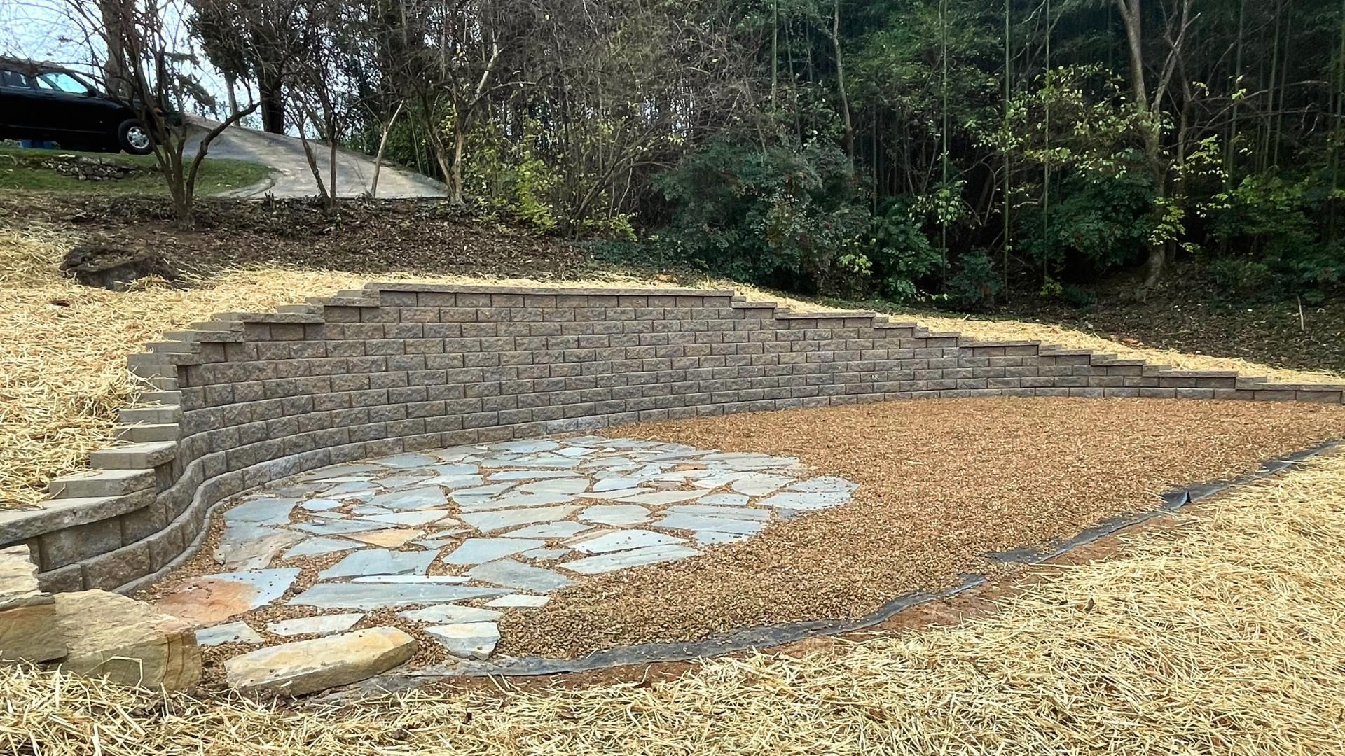A terraced retaining wall built into a sloped landscape, featuring a stone patio and gravel ground covering.