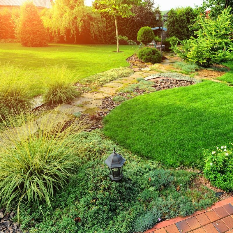 A vibrant green garden with a stone path, manicured lawn, small shrubs, and a lantern, bathed in warm sunset light.