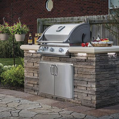 A built-in stainless steel gas grill set into a rustic stone kitchen island on a flagstone patio.