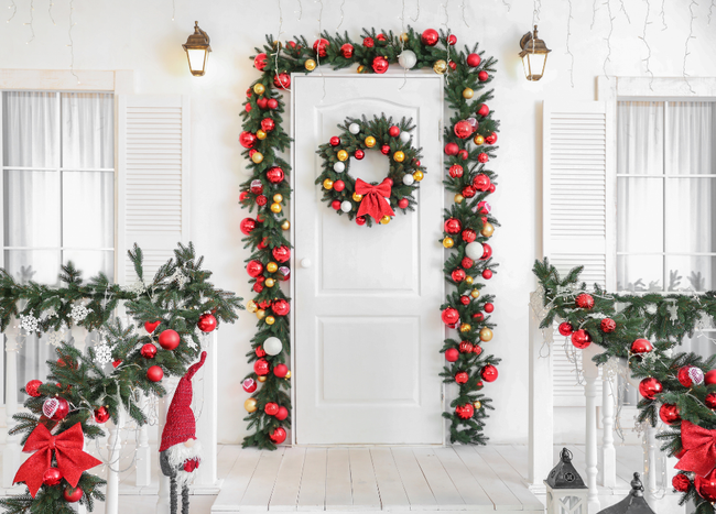 Christmas-decorated white porch with garland, ornaments, wreath on the door, and lights.