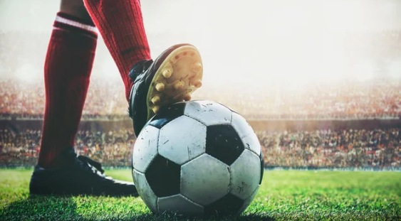 Soccer player’s cleat poised on a ball on a stadium field