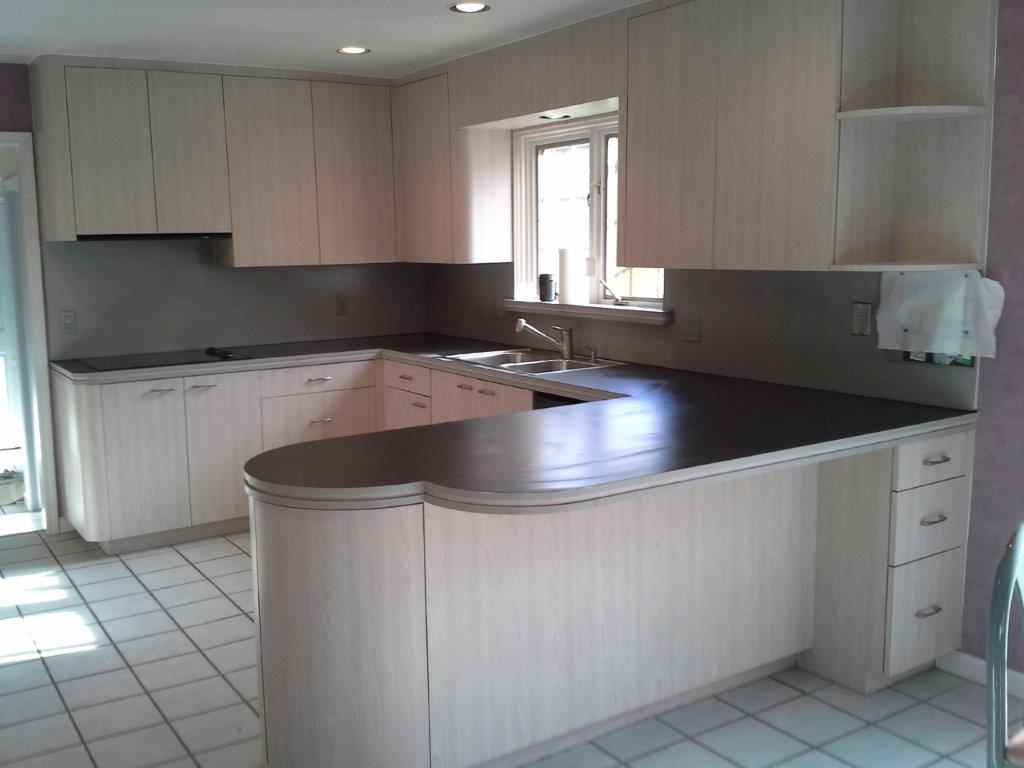 A kitchen with light wood cabinets, dark countertops, a U-shaped peninsula, and white tiled flooring.