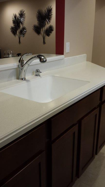 A white bathroom sink with a silver faucet, set in a light countertop above dark brown wooden cabinets.