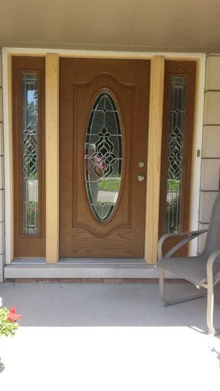 A wood-toned front door with a vertical oval glass pane, flanked by matching sidelights, on a concrete porch.