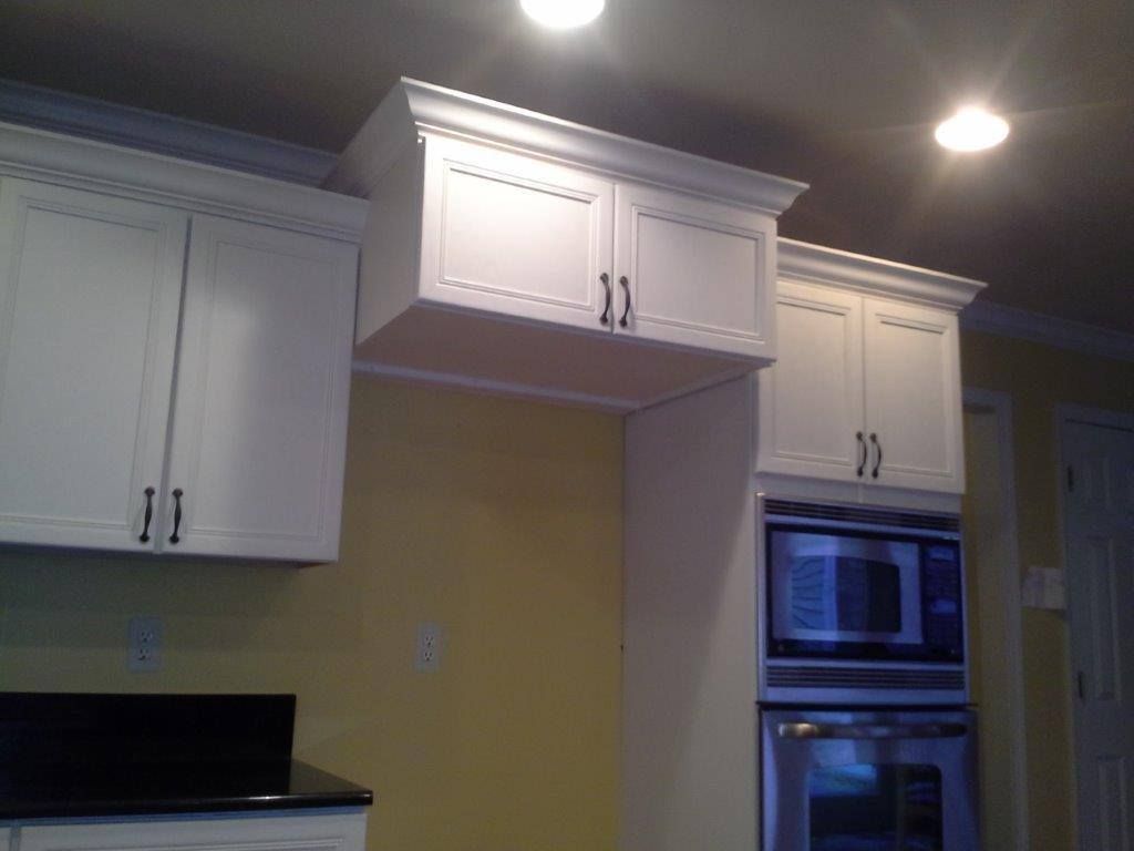 White kitchen cabinets installed above a countertop and a built-in oven with a microwave on a yellow wall.