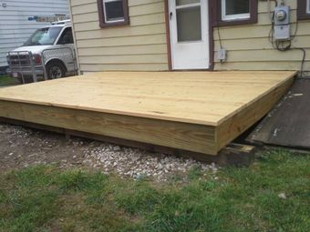 A newly constructed wooden deck sits against a house, resting on concrete blocks over a gravel yard.