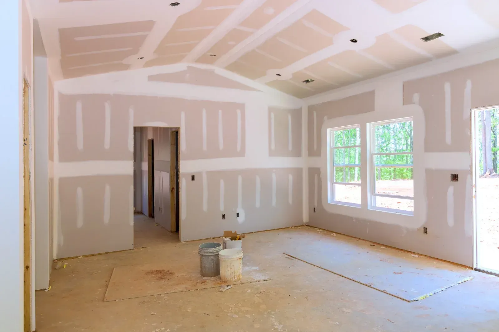 An interior room under construction with newly installed drywall, taped seams, and two buckets on the floor.