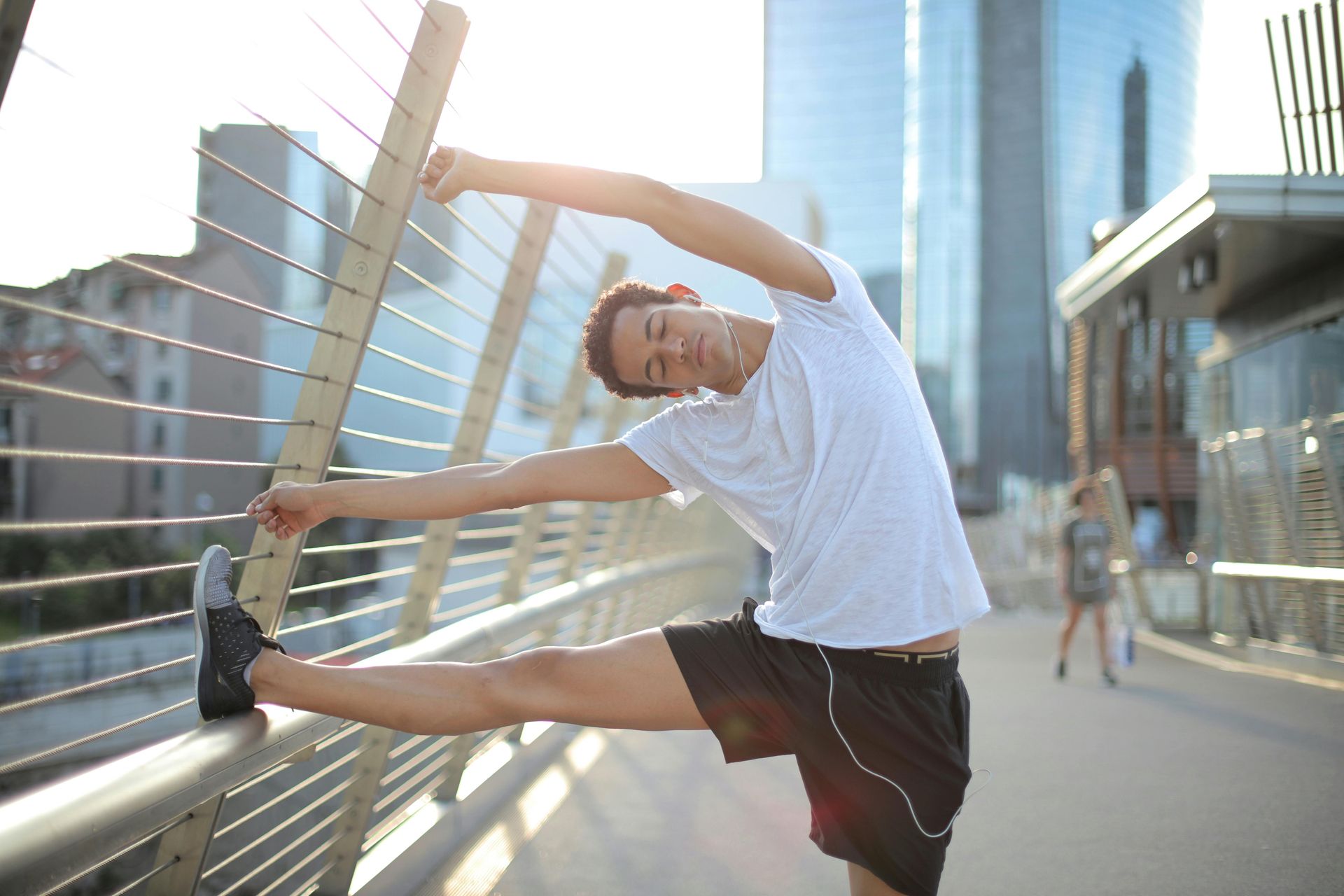 A man is stretching his legs on a bridge in the city.