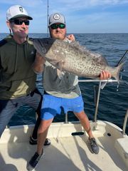 Two men are standing on a boat holding a large fish.