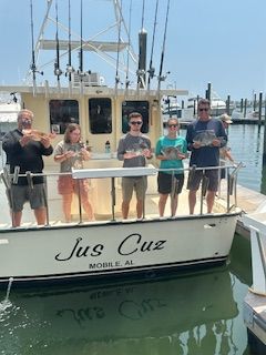 A group of people are standing on the deck of a boat called jus cuz.
