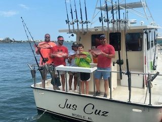 A group of people are standing on a boat called jus cuz