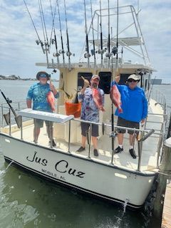 Three men are standing on a boat holding fish.