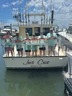 A group of people are standing on the back of a boat holding fish.