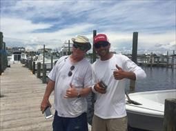 Two men are standing next to each other on a dock giving a thumbs up.
