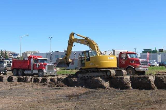 Une excavatrice jaune creuse un trou dans un champ de terre à côté d'un camion à benne rouge.