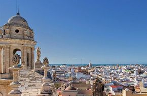 A large building with a dome sits on the shore of a body of water in Cadiz