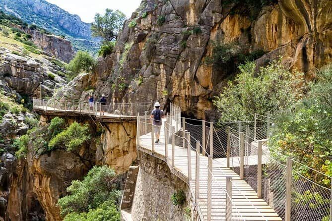 A group of people are walking across a bridge between two cliffs.