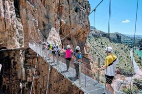 A group of people are standing in Caminito del rey on a bridge between two cliffs.