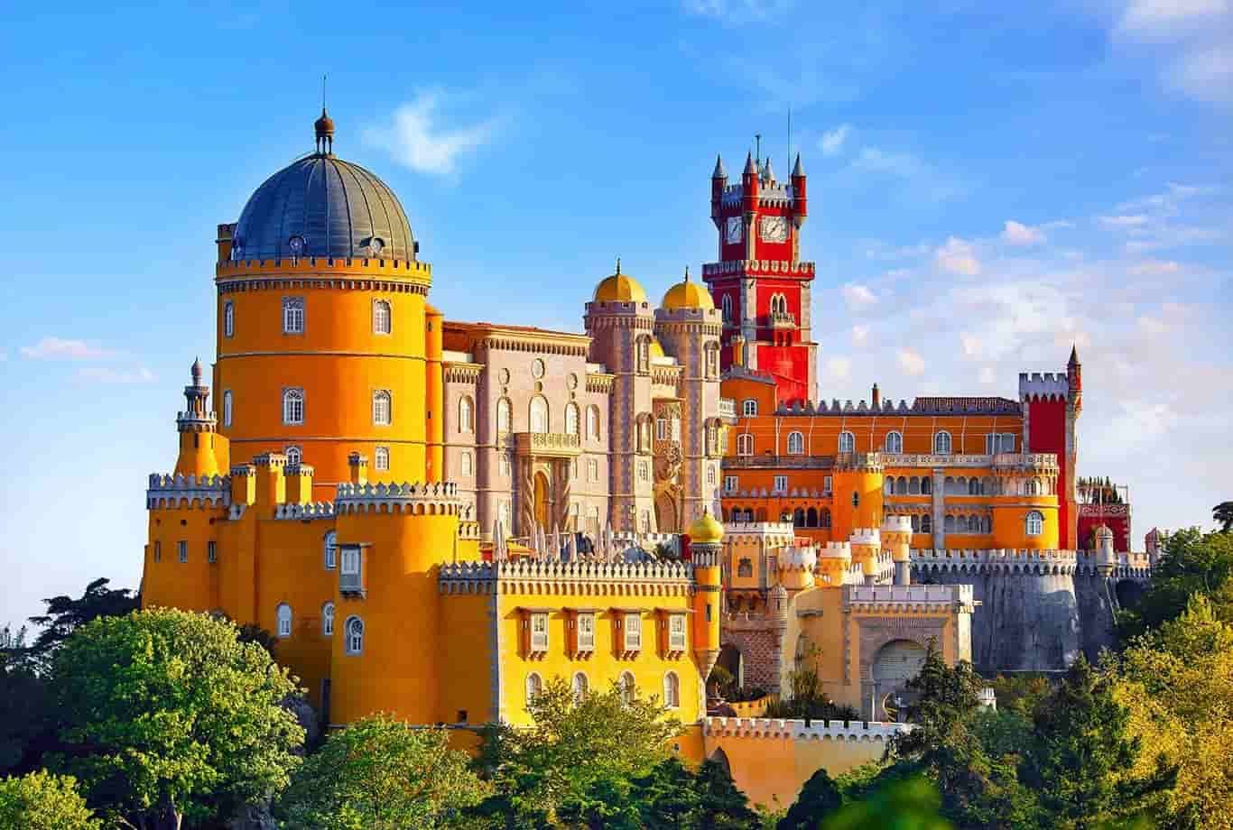 A large yellow and red castle in Sintra is surrounded by trees and a blue sky.