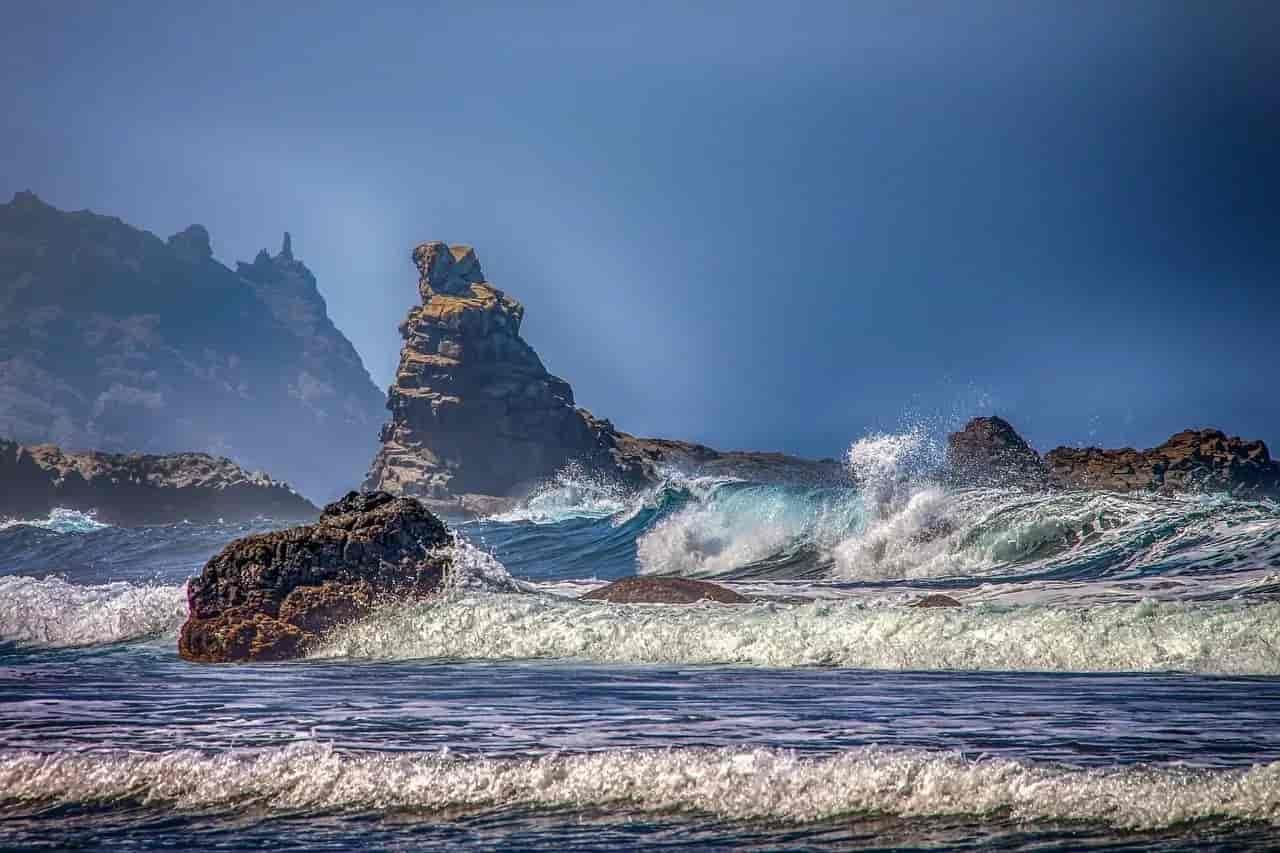 A large rock formation in the middle of the ocean with waves crashing against it.
