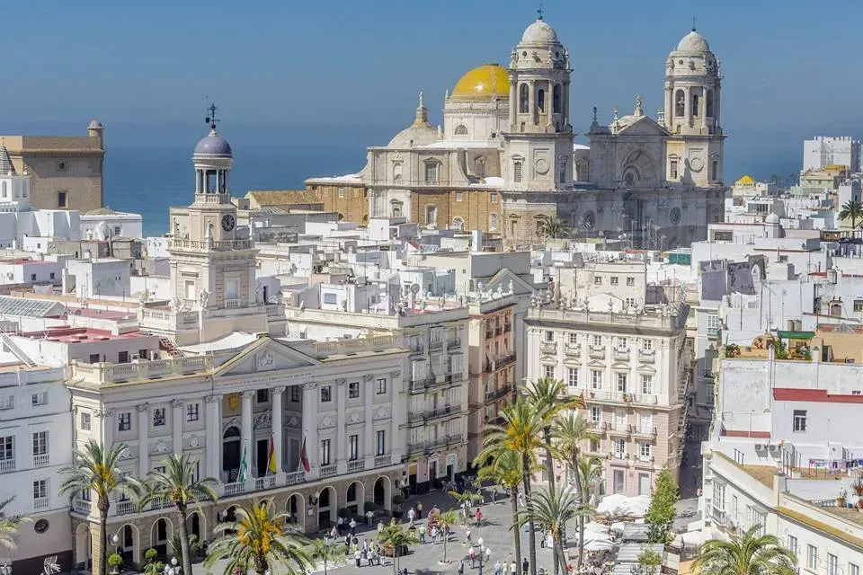 A large Cadiz building with a dome sits on the shore of a body of water