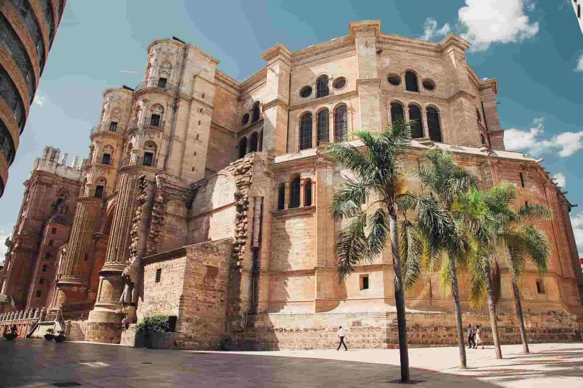 A fountain in the middle of Malaga square surrounded by buildings and palm trees.