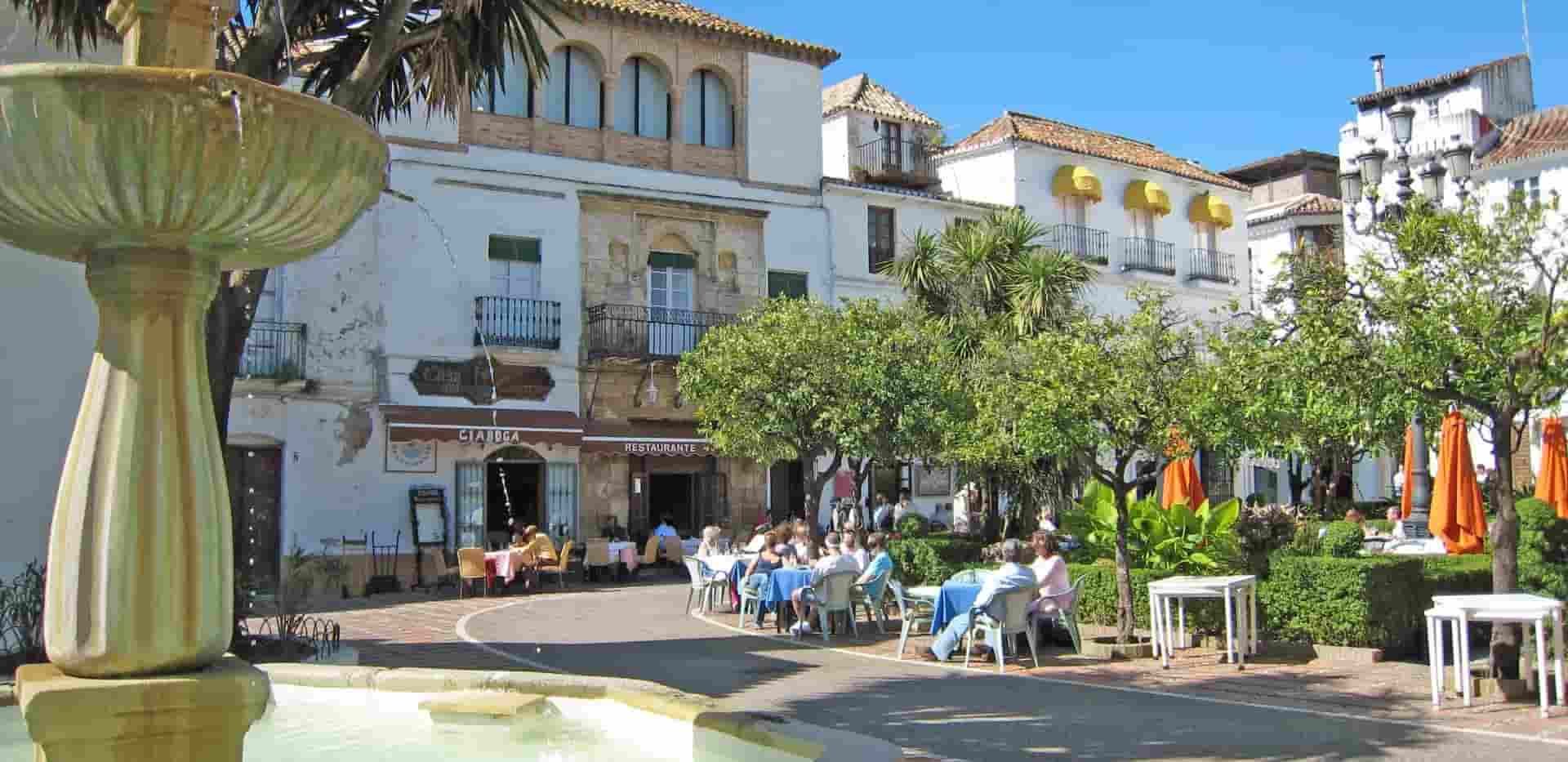 A fountain in front of a building with people sitting at tables in Marbella