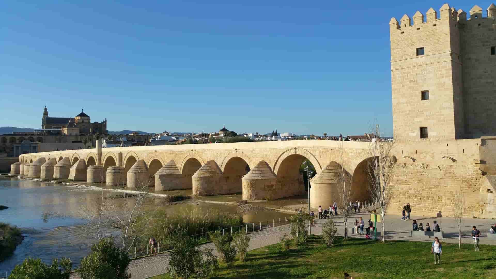 There is a bridge over a river in the foreground and Cordoba in the background.
