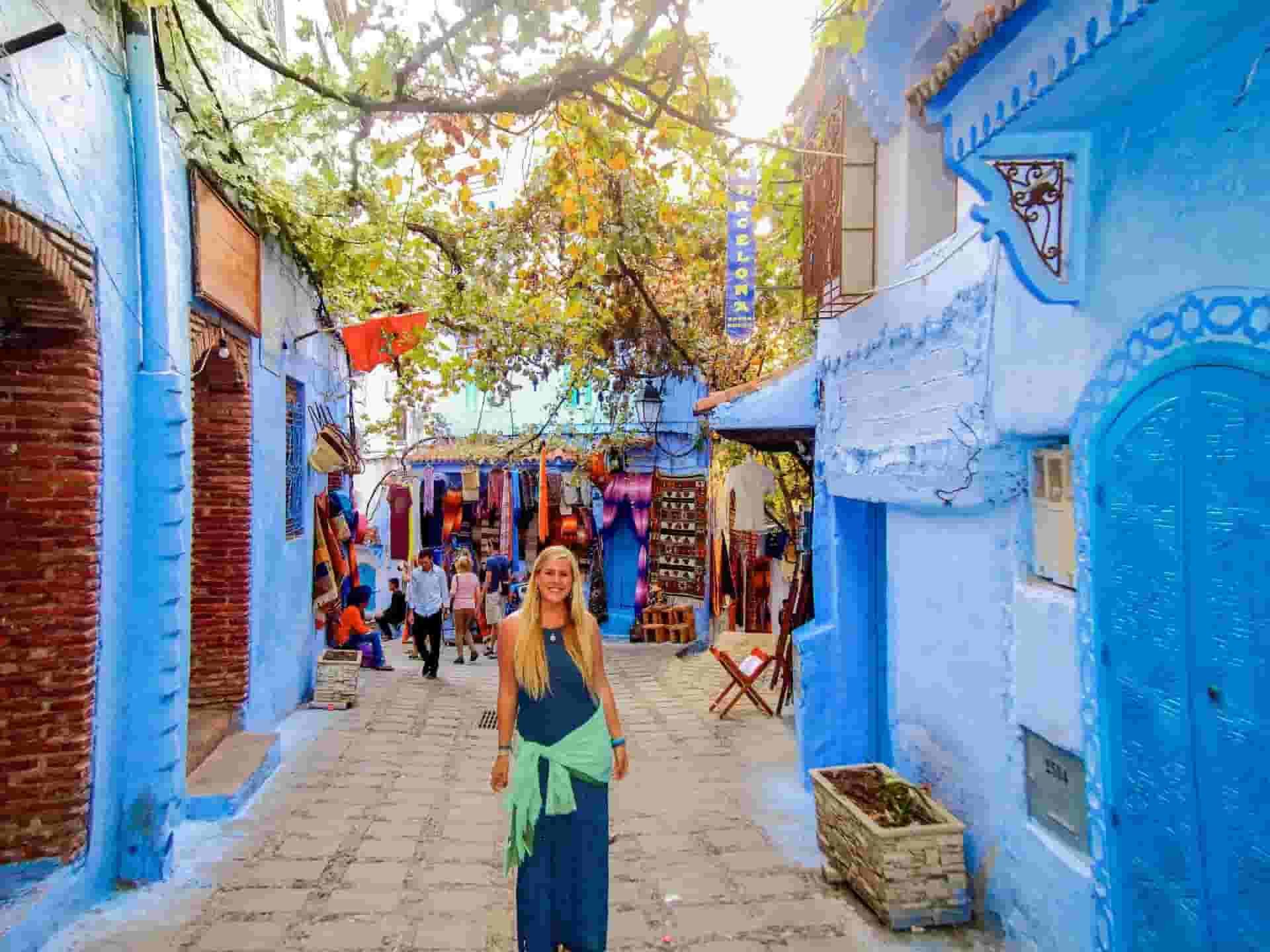 A woman is standing in a narrow street in Tangier between two blue buildings.